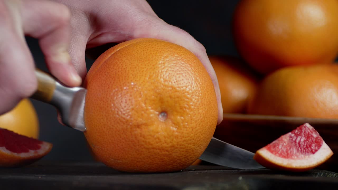 Male hand with a knife cut a ripe grapefruit.