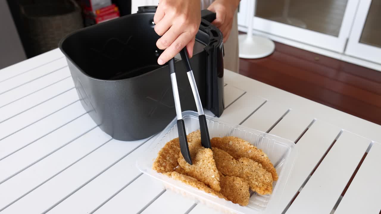 A person places breaded chicken into an air fryer basket on a white table