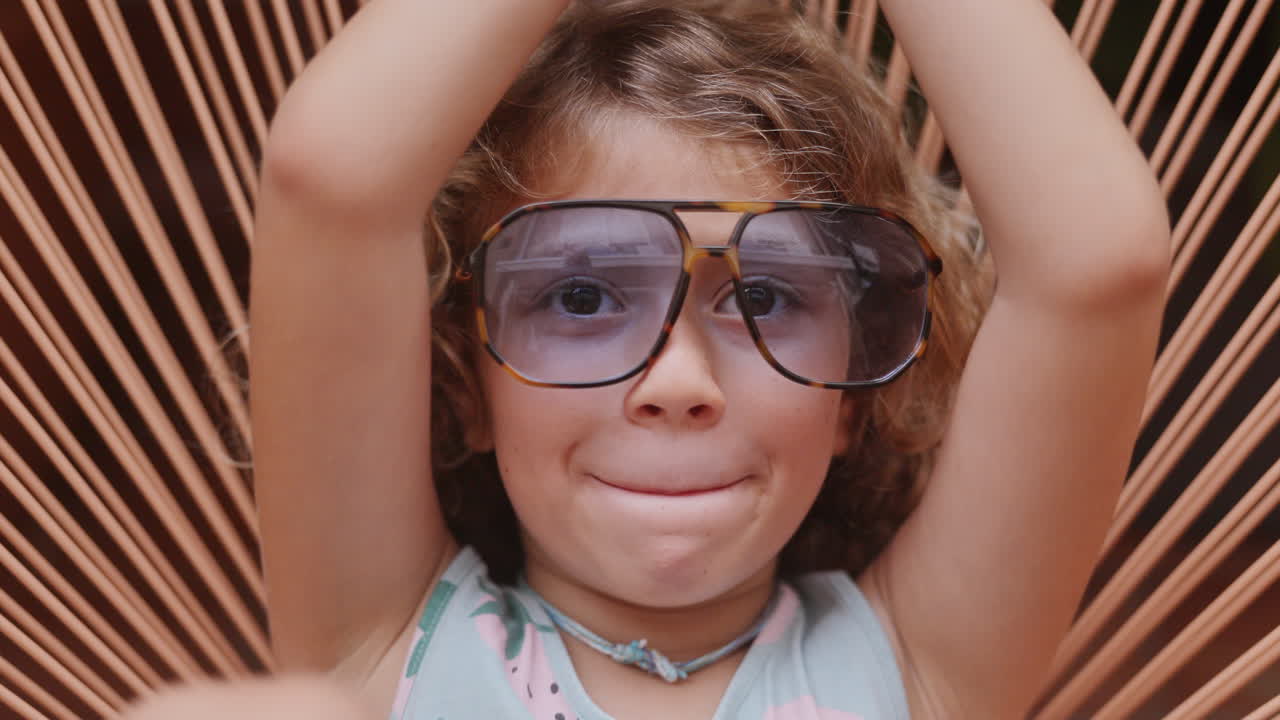 Cool little girl in a garden chair with sunglasses making faces