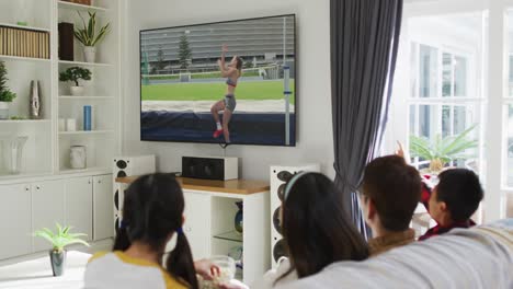 Composite-of-happy-family-sitting-at-home-together-watching-athletics-high-jump-event-on-tv