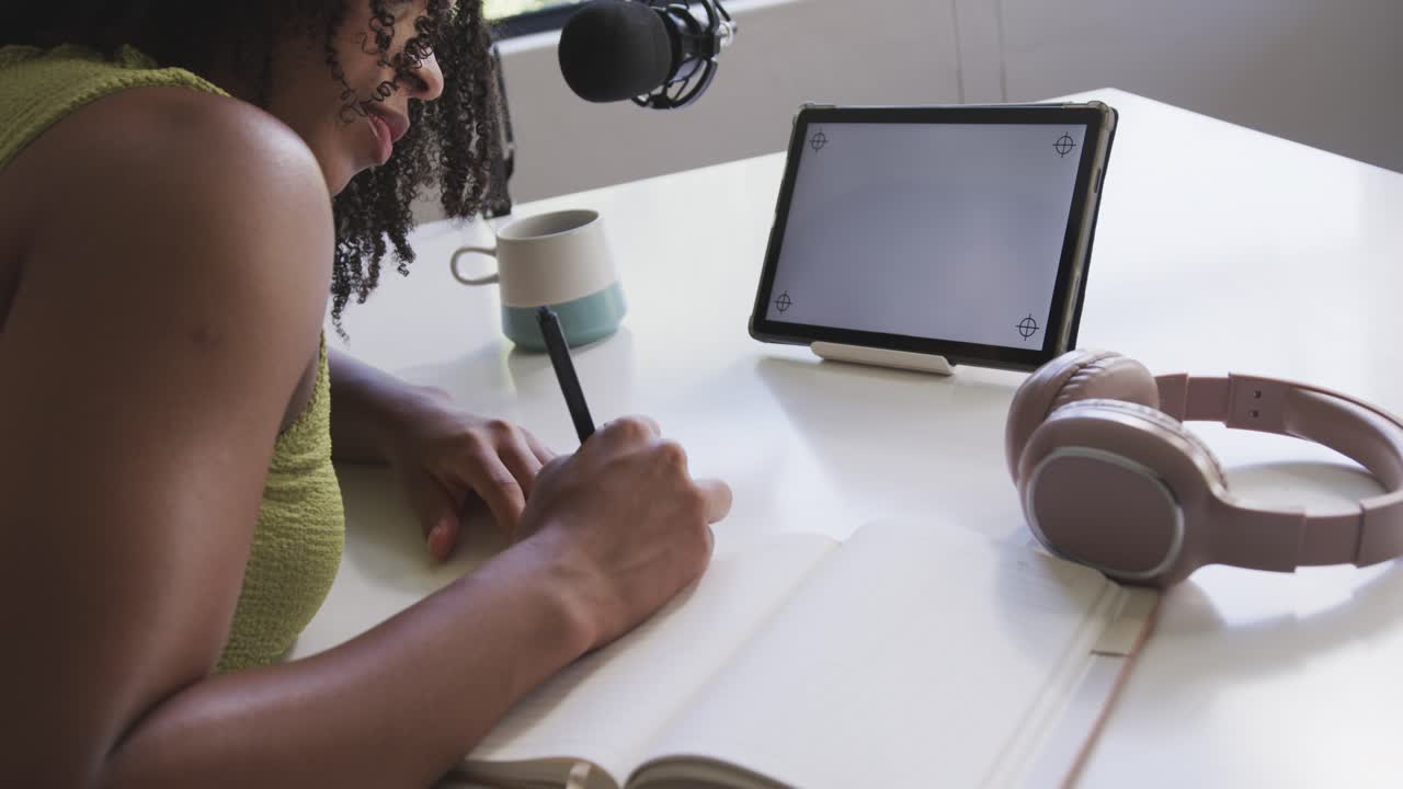 Leaning forward, woman is writing in notebook with black pen by window, flipping pages for mic
