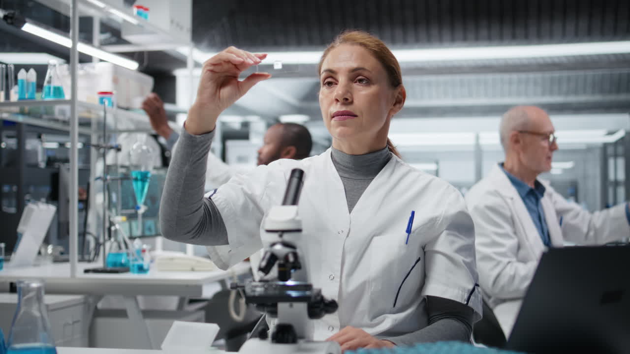 Materials scientist inspecting thin glass slide for structural defects in lab