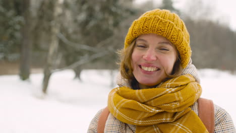 close up view of a smiling woman looking smartphone and around in winter forest