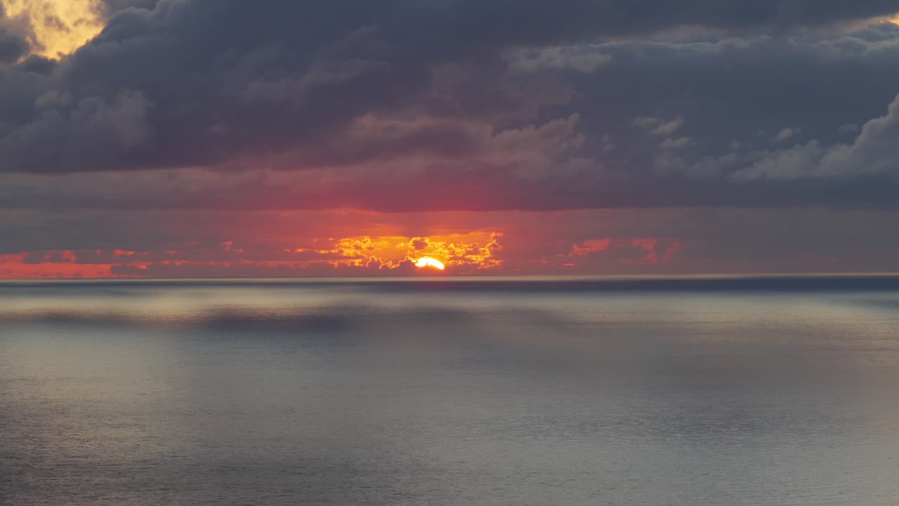 Dramatischer Sonnenuntergang über dem Ozean, die Sonne bricht durch dunkle Wolken. Drohnenaufnahme, Textfreiraum.