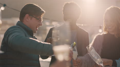 happy group of friends celebrating rooftop party drinking alcohol young man pouring champagne enjoying reunion celebration at sunset