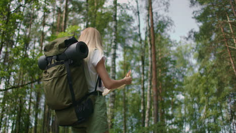 slow motion back view: young caucasian woman looking for direction on a map while hiking in the forest. happy girl while hiking in nature and orienteering with help of a map