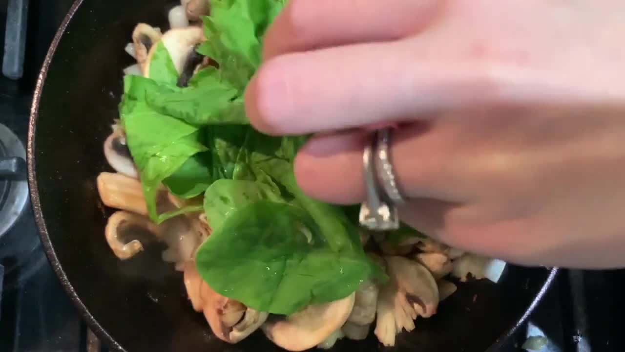주철 프라이팬을 사용하여 버섯, 양파, 녹색 시금치 요리