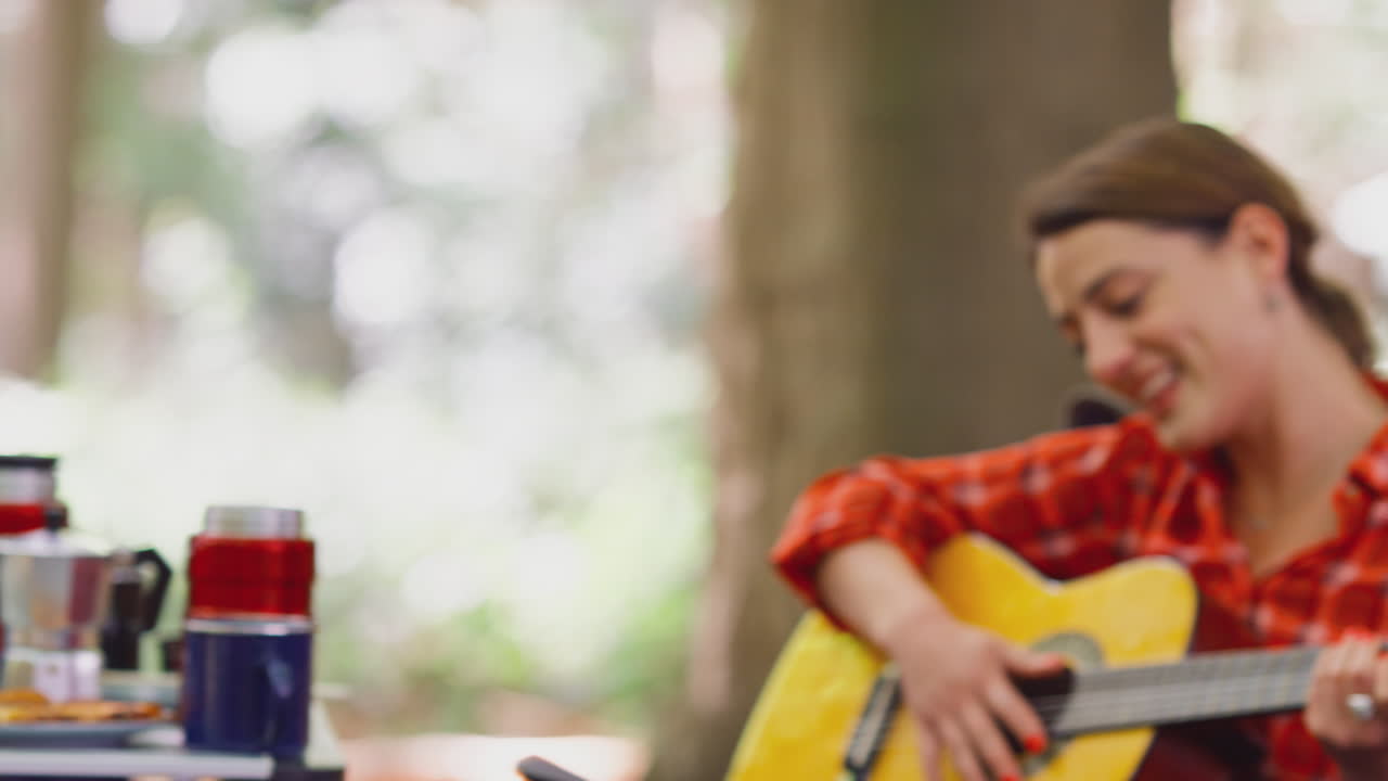 Grupp av kvinnliga vänner på campingsemester i skogen som äter och sjunger till gitarr