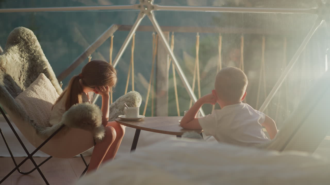 아이들은 글램핑 텐트에서 일찍 휴식을 취합니다. 형제자매들은 유리  아래 주변의 평화로움을 맛보며 테이블에 앉아 있습니다. 슬픈 아이들은 창문을 통해 쳐다보고 있습니다.