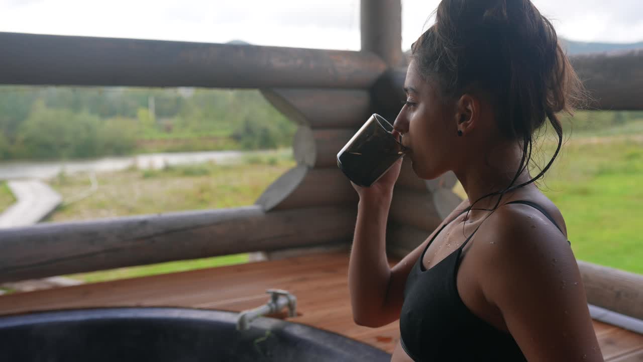 Woman enjoying a drink by a hot tub in a log cabin overlooking a river