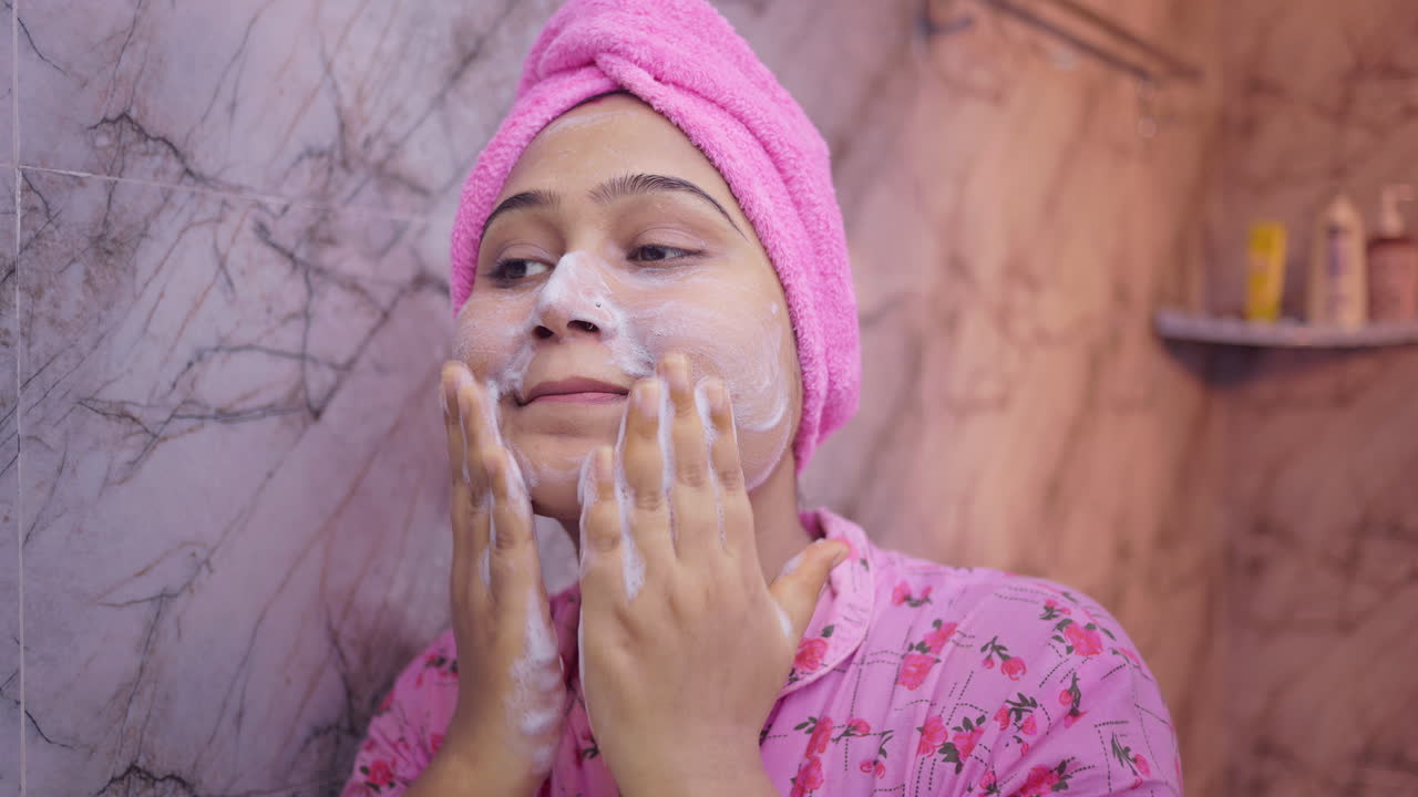 Young lady cleaning her face with cleanser during her morning skincare routine, wearing night dress in bathroom