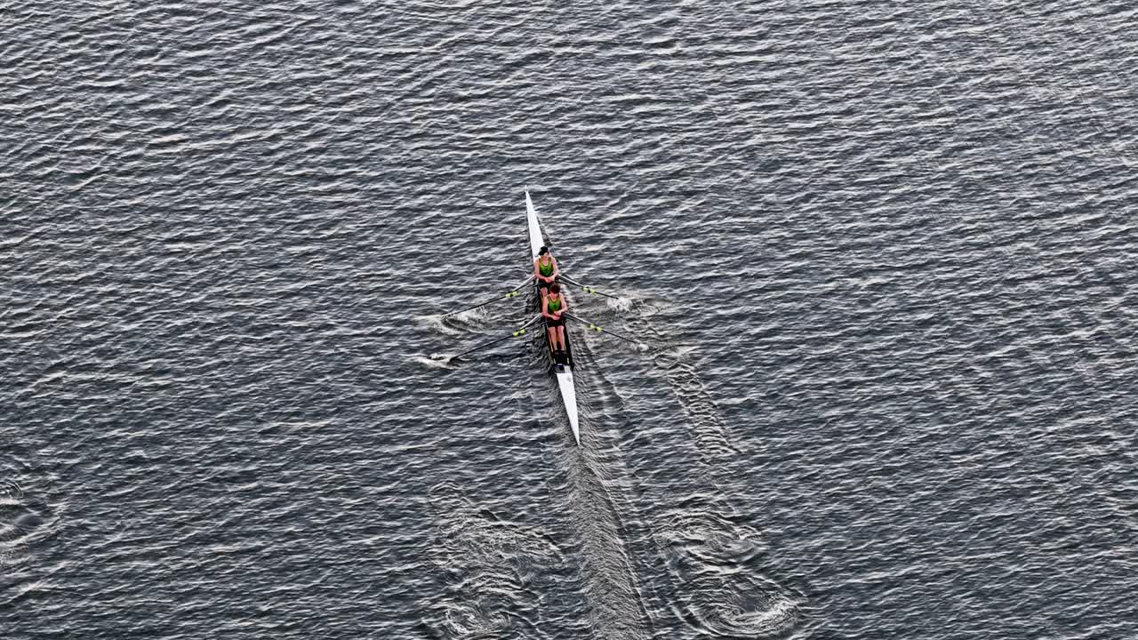 Drone captures athletes rowing in sync on calm waters, showcasing teamwork and precision under natural light
