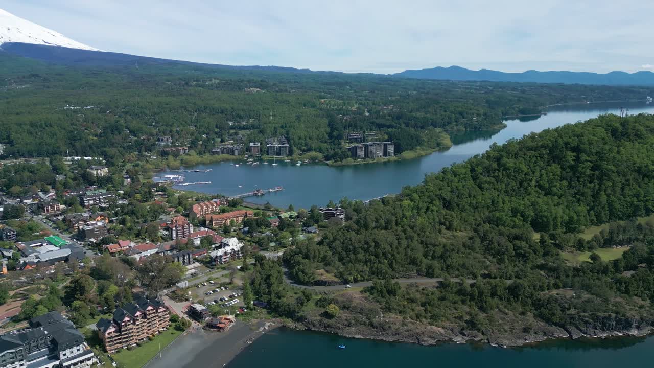 Panoramic drone view over Pucón, Chile showing lakeside town, lush hills, and distant lake horizon under a clear sky