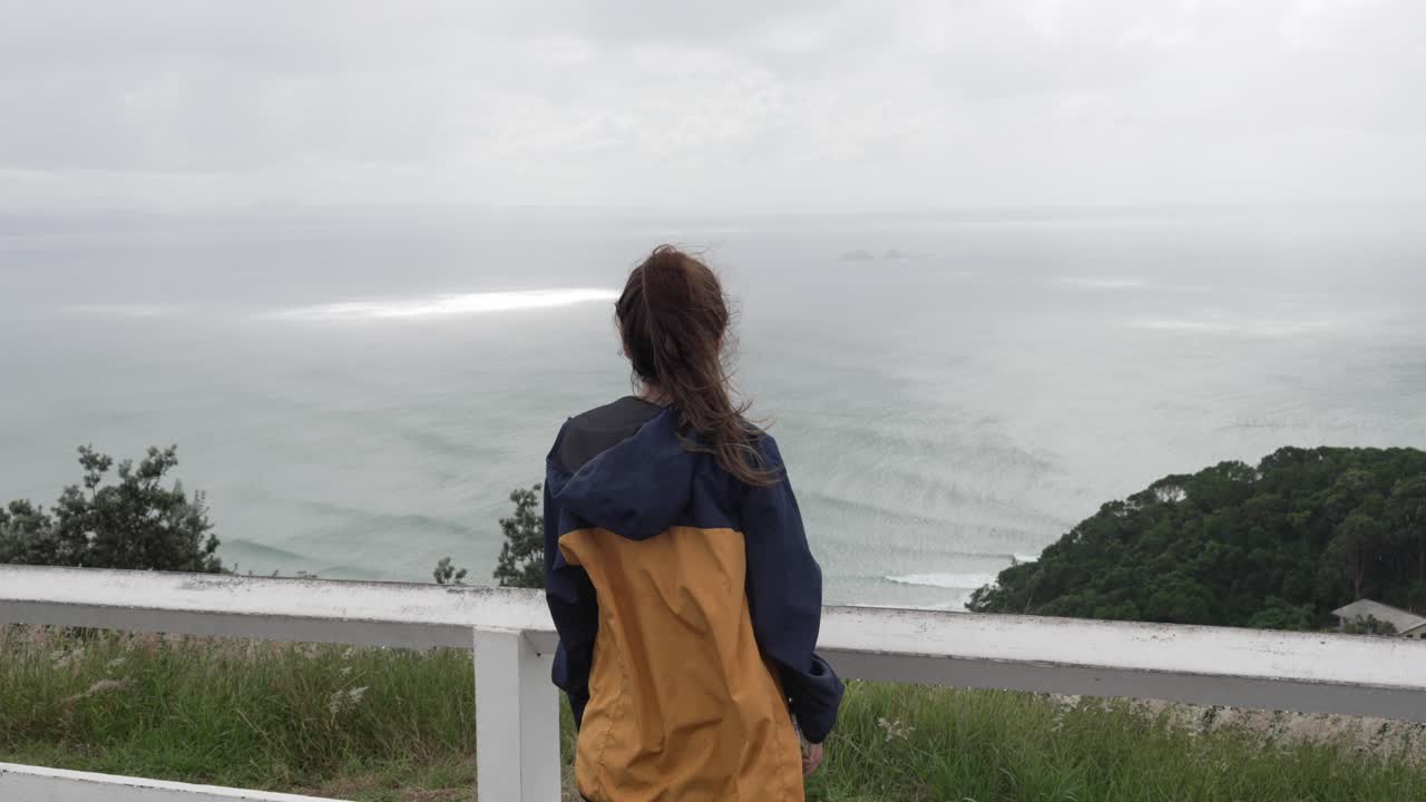 Looking at ocean waves, young brunette woman overlooking relaxing landscape