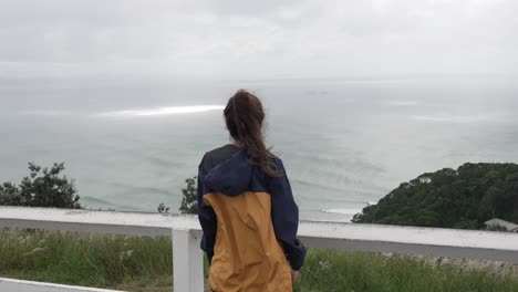 looking at ocean waves, young brunette woman overlooking relaxing landscape