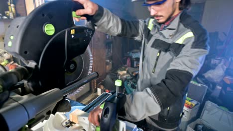 a young man with a beard in gray overalls by profession a carpenter works with a circular cutting machine in his home workshop