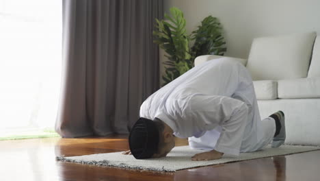 asian muslim man reciting surah al-fatiha passage of the qur'an, in a daily prayer at home in a single act of sujud called a sajdah or prostration