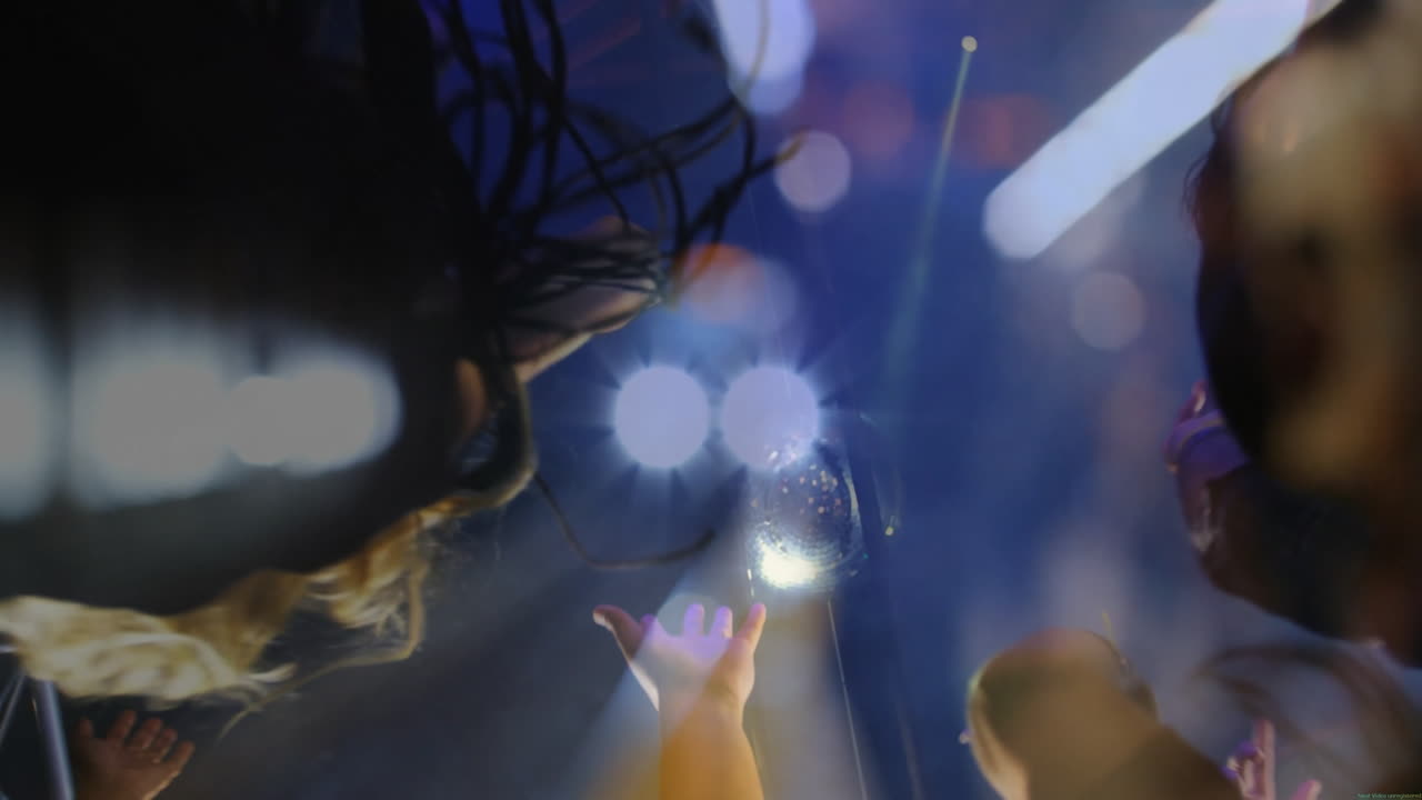 Female performer crowd surfing over audience hands while spotlights dancing in disco ball haze
