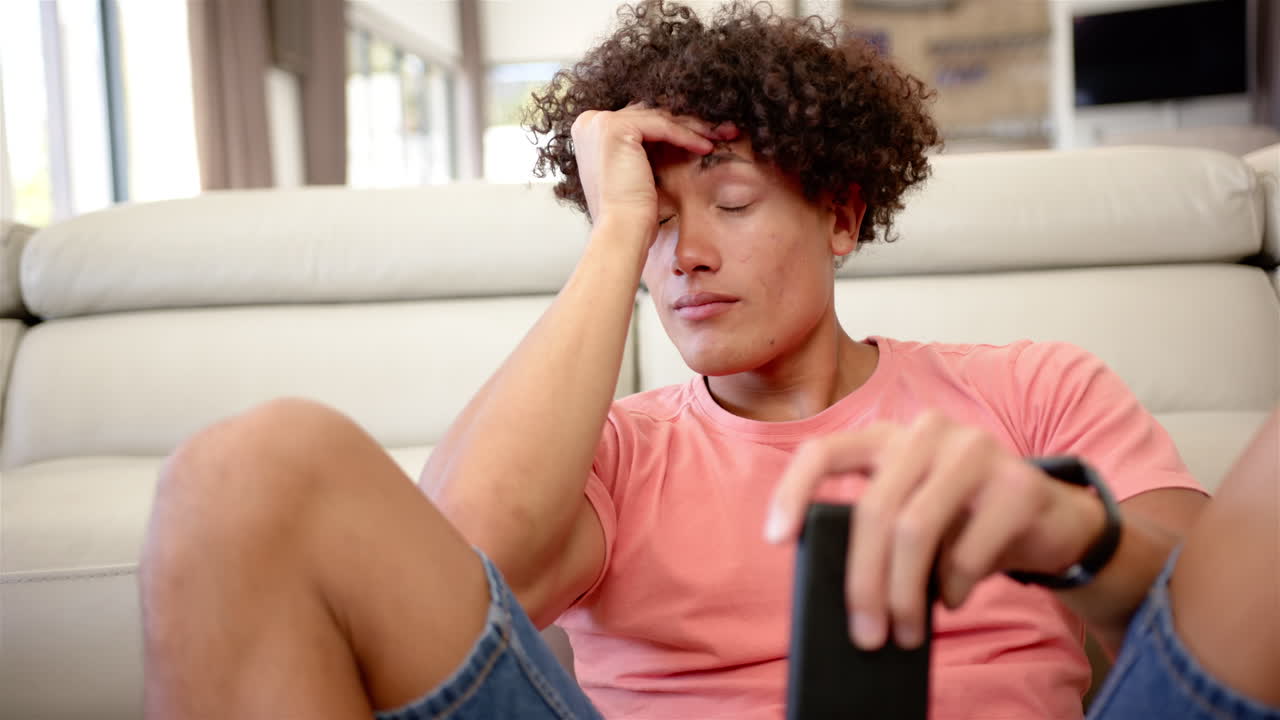 A young biracial upset and stressed man looks tired, holding a remote