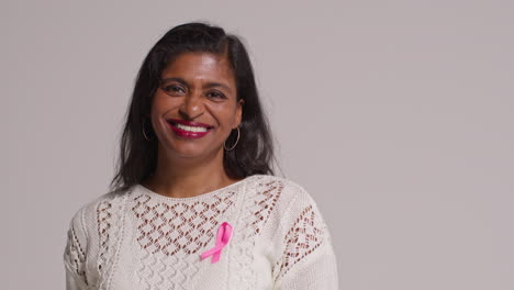 Studio-Portrait-Of-Smiling-Mature-Woman-Wearing-Pink-Breast-Cancer-Awareness-Ribbon-Against-White-Background-2