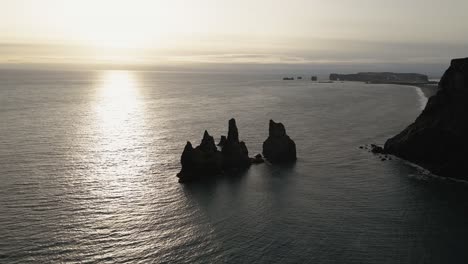 Rock-formations-in-the-water,-Reynisdrangar-Seastacks,-against-the-backdrop-of-Reynisfjara-Black-Sand-Beach-near-the-village-of-Vik-in-Iceland