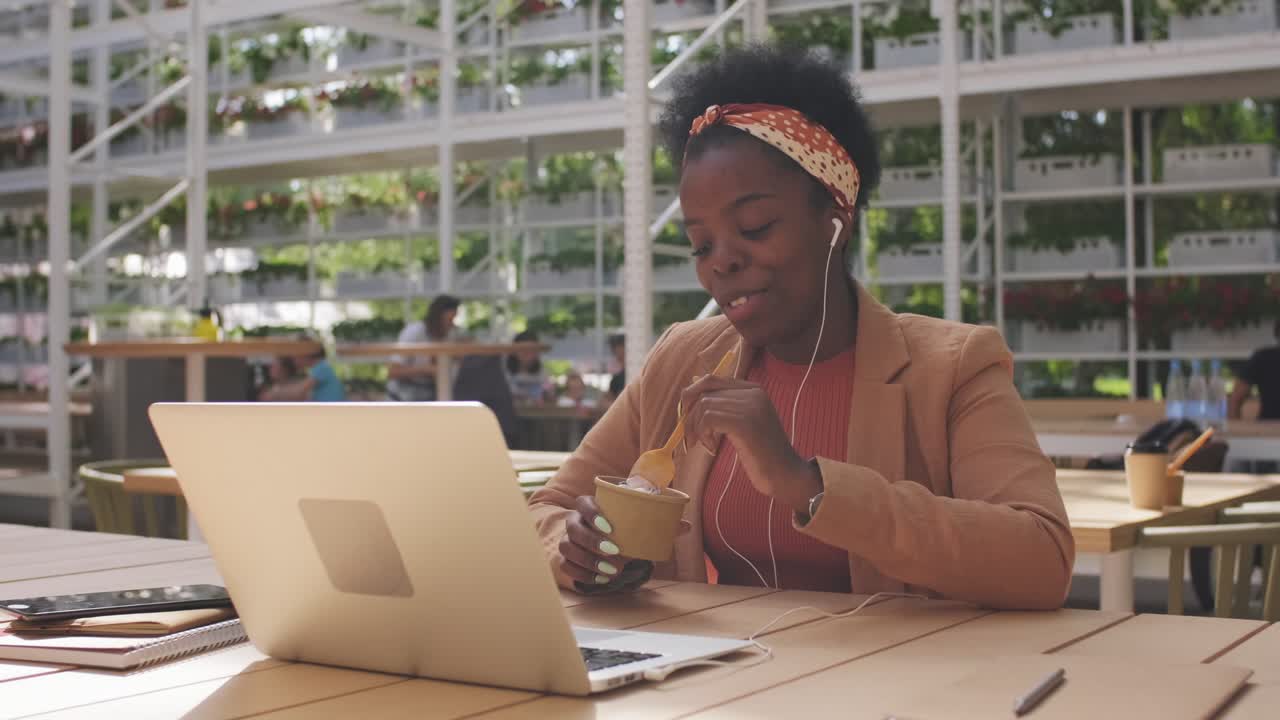 Woman Eating Ice Cream Sitting On Bar Terrace While Talking On Videocall Wearing Headphones