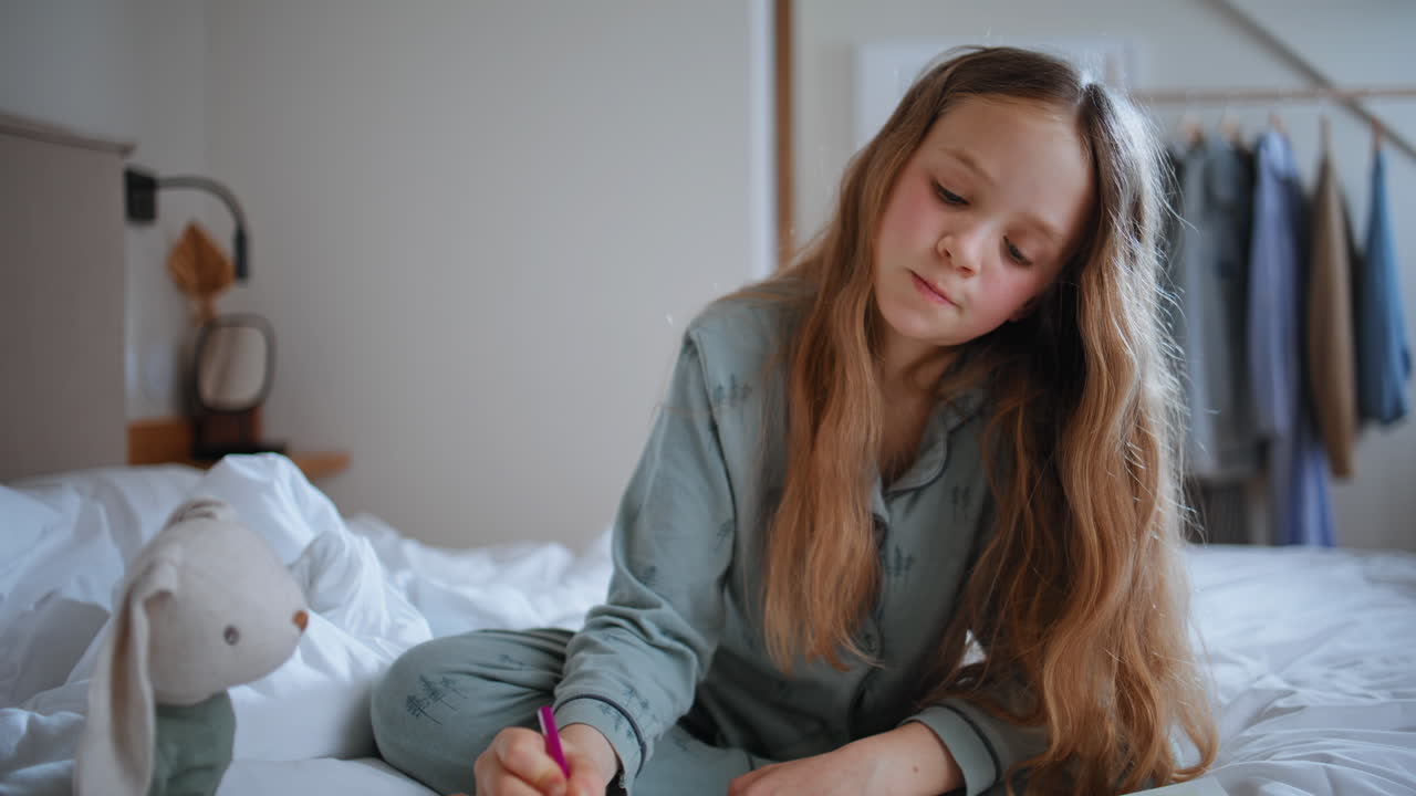 Creative girl doing arts sitting white mattress indoors. Cute child painting