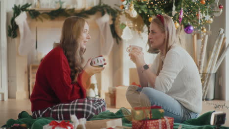 hermanas hermosas hablando mientras sostienen tazas de café durante la navidad en casa