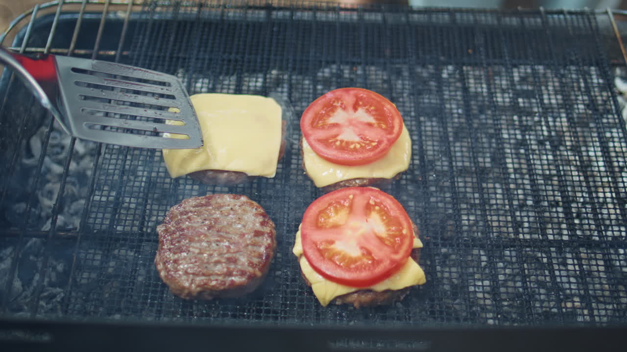 Closeup hand adding tomato cheese to burger patties on grill at park picnic