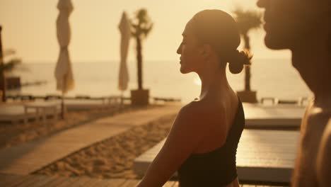 Una-Chica-Morena-Con-Un-Uniforme-Deportivo-Negro-De-Verano-Está-Meditando-Con-Un-Chico-En-La-Playa-Junto-Al-Mar-Durante-Un-Amanecer-Dorado