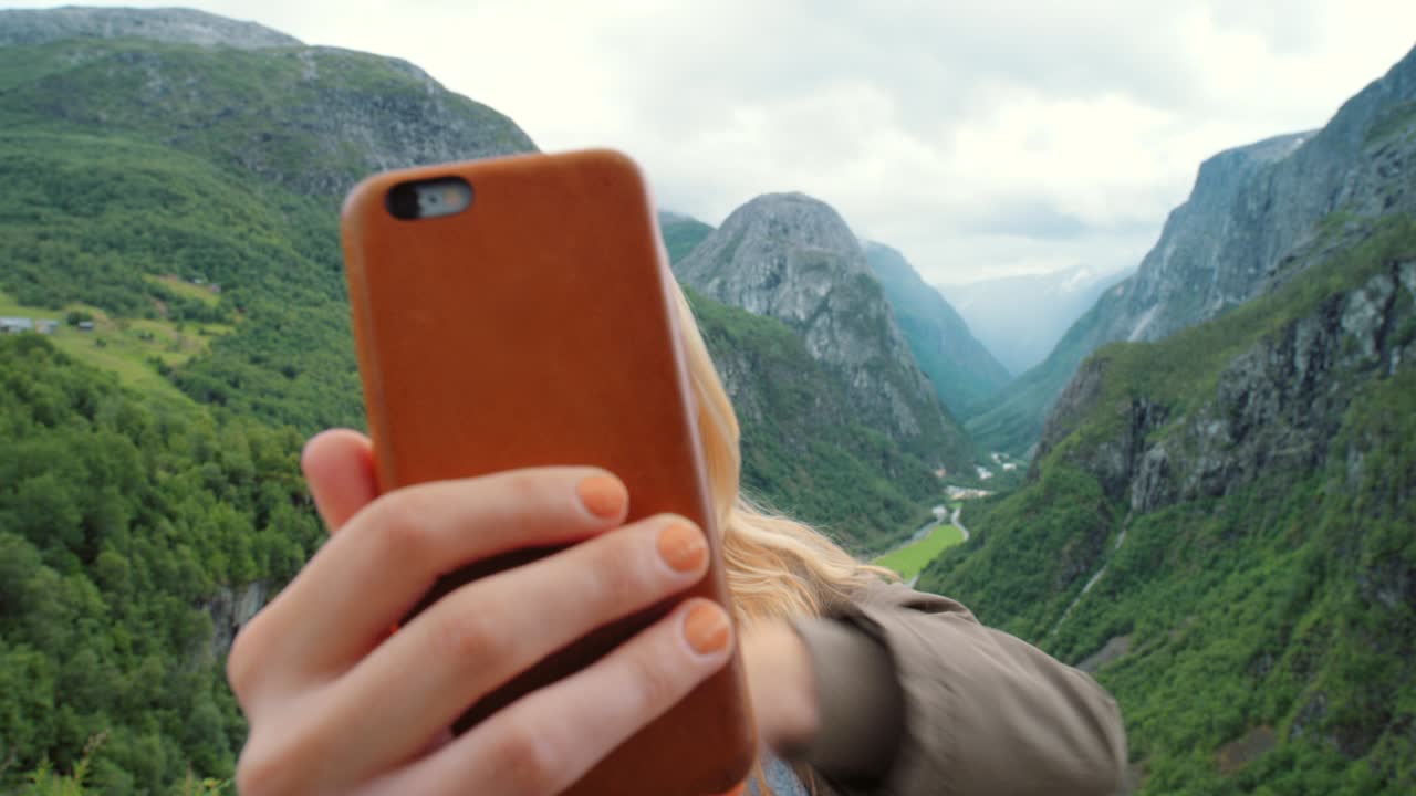 imágenes de video de 4k de una joven de pie y usando su teléfono celular para una llamada de video mientras explora el valle de naeroydalen