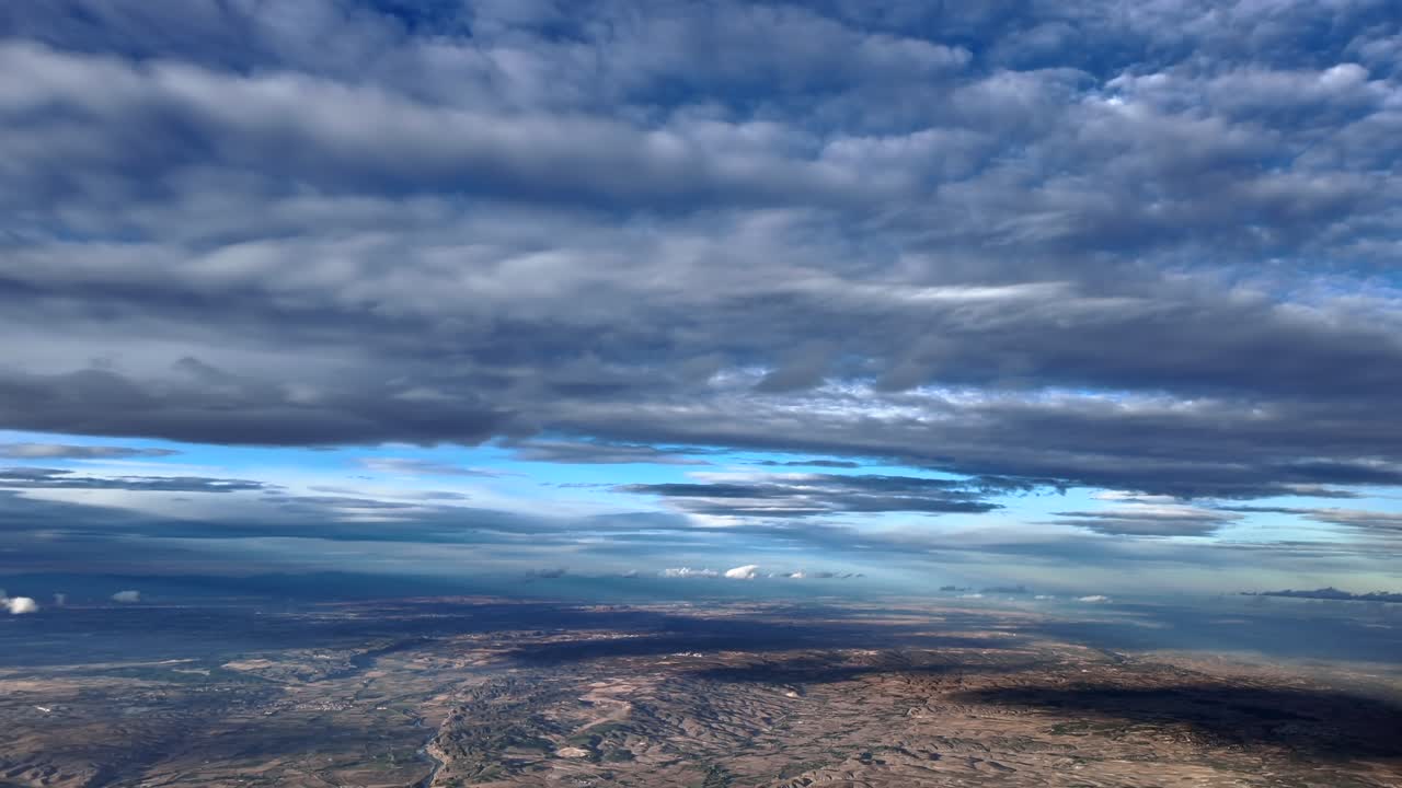 An immersive pilot’s view from a jet cockopit flying at supersonic speed beneath a flat landscape bathed by the sunlight piercing the stratus clouds