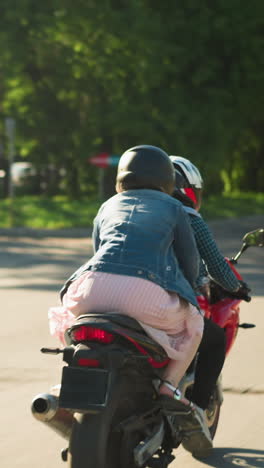 back view of two friends riding a power bike behind a black jeep and a white car seen ahead, the road is flanked by green trees and electric poles