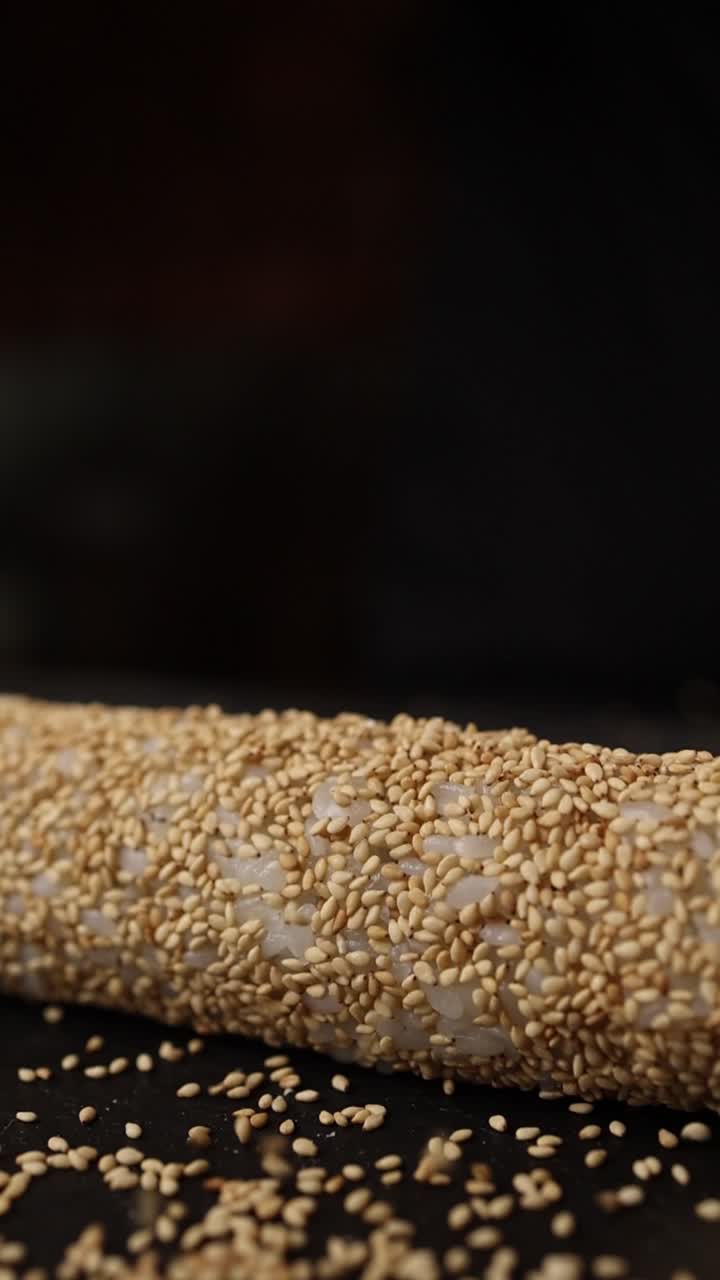 preparando un rollo de sushi cubierto de sésamo