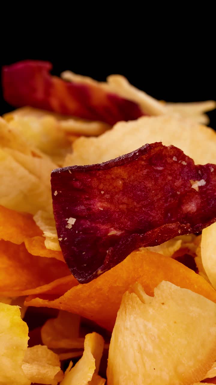 Chips coloridos de vegetais de raiz giram sob iluminação de estúdio, destacando texturas crocantes e cores vibrantes.