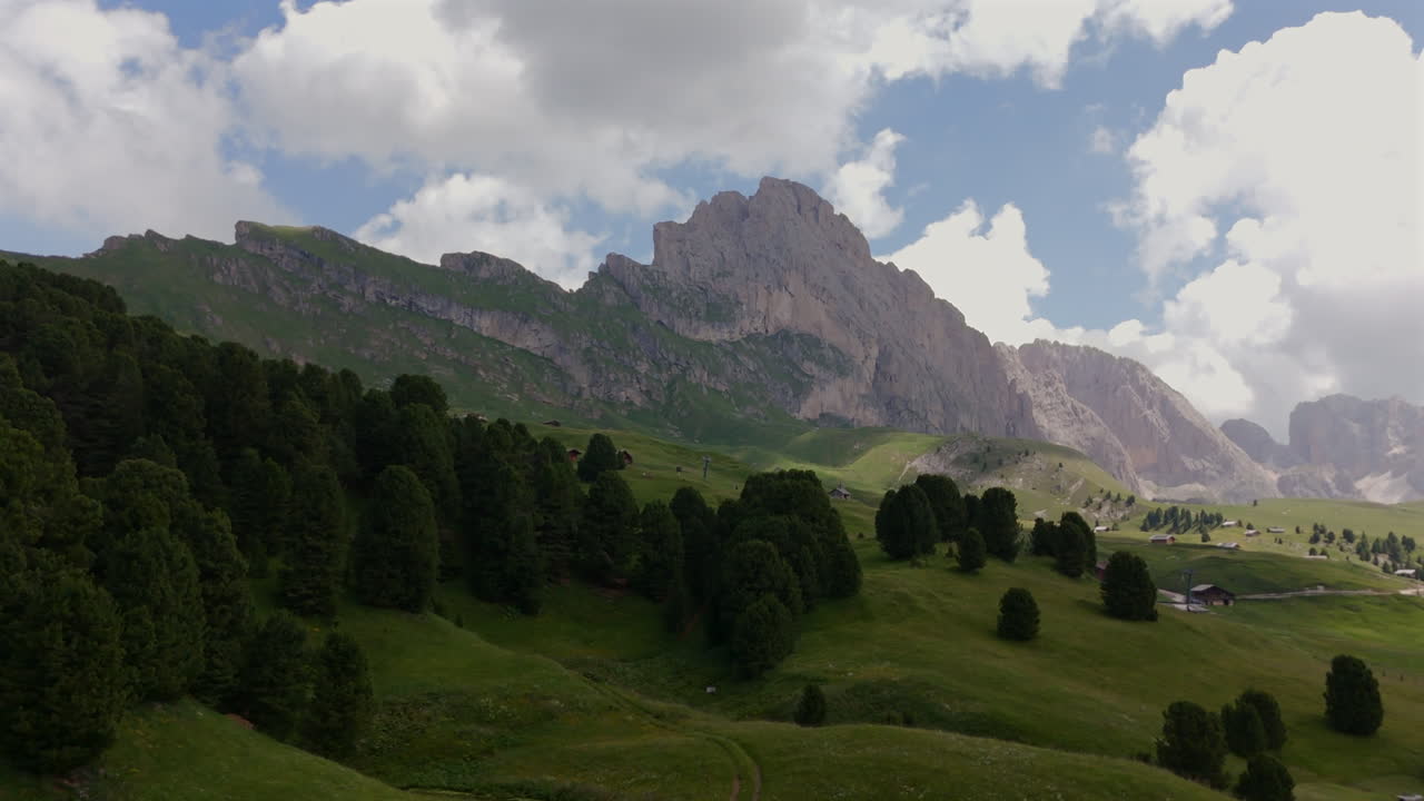 울창한 초록 잔디에 자리 잡은 알파인 마을의 경치가 아름답고, 울창한 숲과 높은 산맥으로 둘러싸여 있으며, 부분적으로 구름이 가득한 하늘 아래 있습니다.