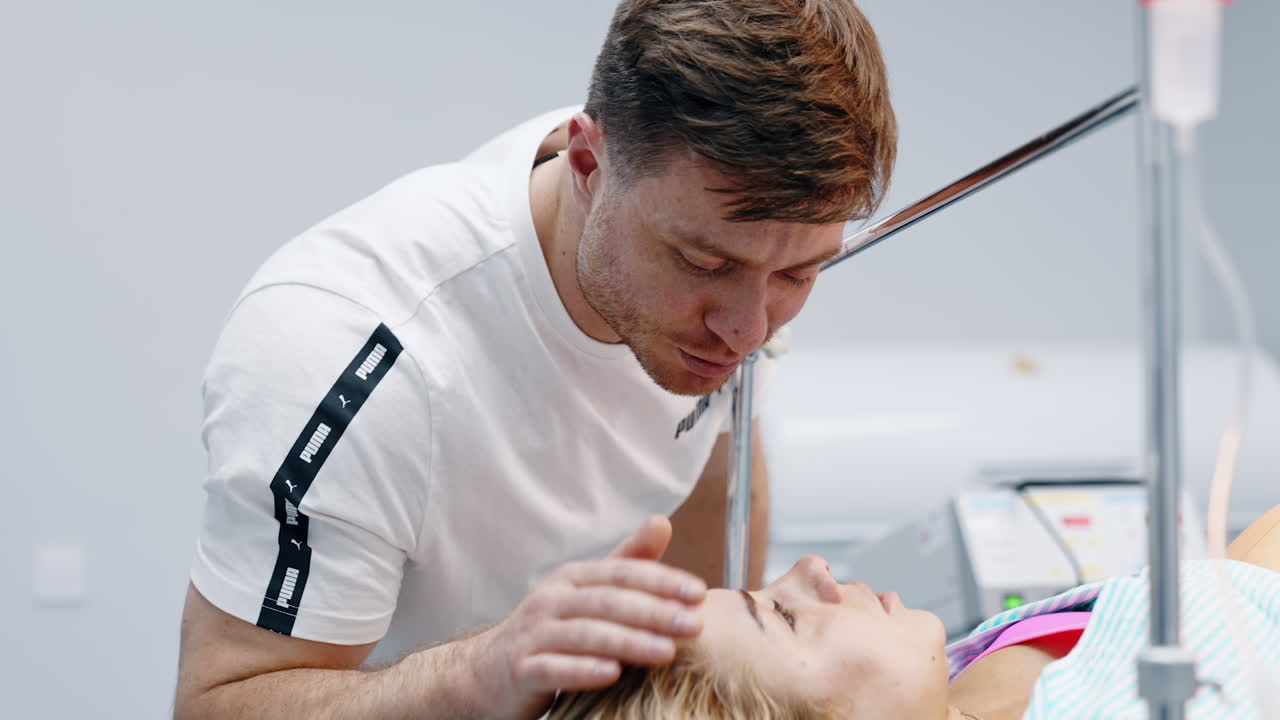 Loving man soothes his wife lying on the operational table. Husband strokes head of woman before C-section surgery.