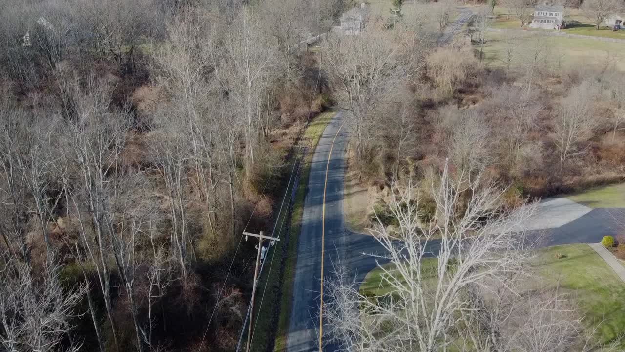 노란색 선으로 도로를 따라 날아가는 드론은 잎이 없는 나무와 땅 위의 전선도 볼 수 있습니다.