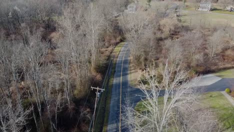 drone flying along a road with a yellow line you can also see trees without leaves and a power line above the ground