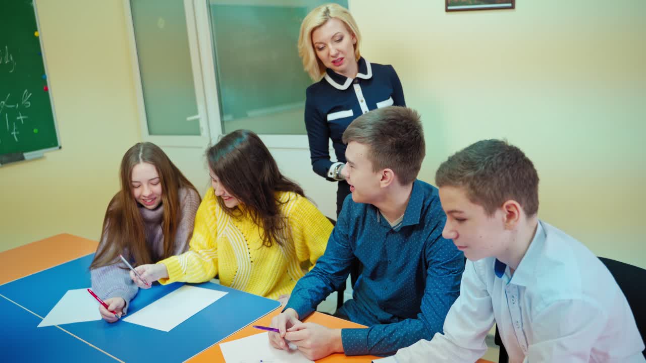 Learning process in middle school. Teen students sitting in the classroom. Positive teacher talking to a boy student. Education concept.