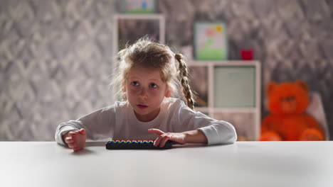 smart little girl with toy abacus does sums sitting at table