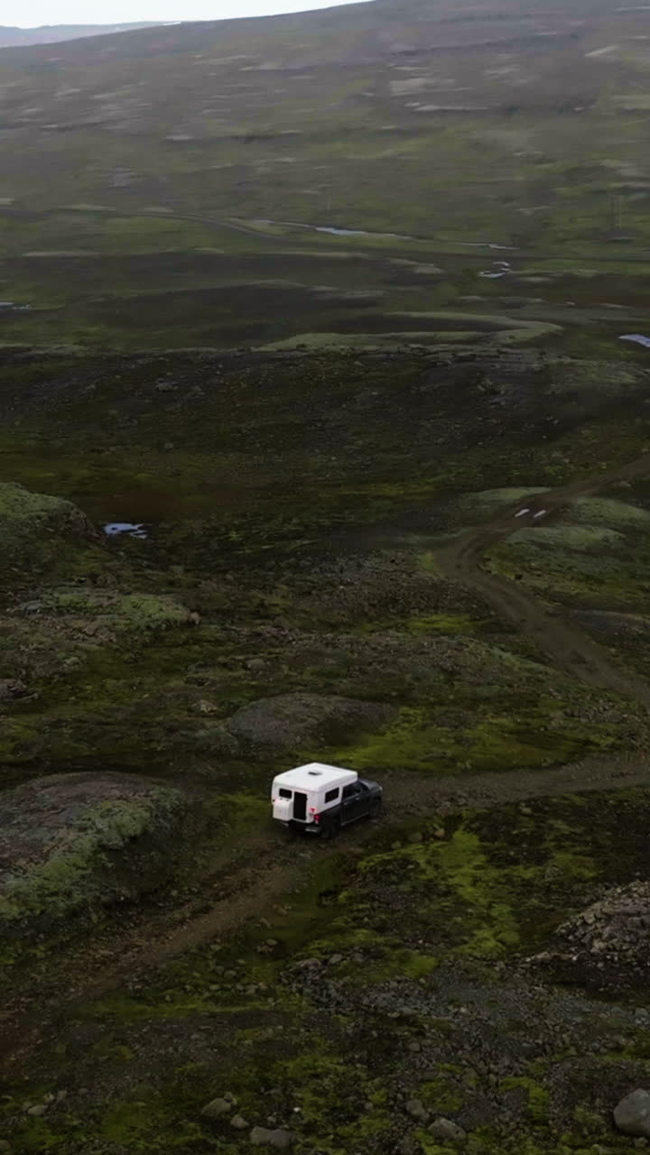 Vertikalt droneoptagelse omkring en autocamper, der kører i Islands vildmark