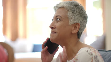 Happy-senior-biracial-woman-sitting-on-couch-and-talking-on-smartphone-at-home,-slow-motion