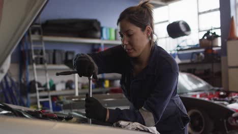 mecánica femenina usando una llave inglesa para reparar un coche en una estación de servicio de automóviles