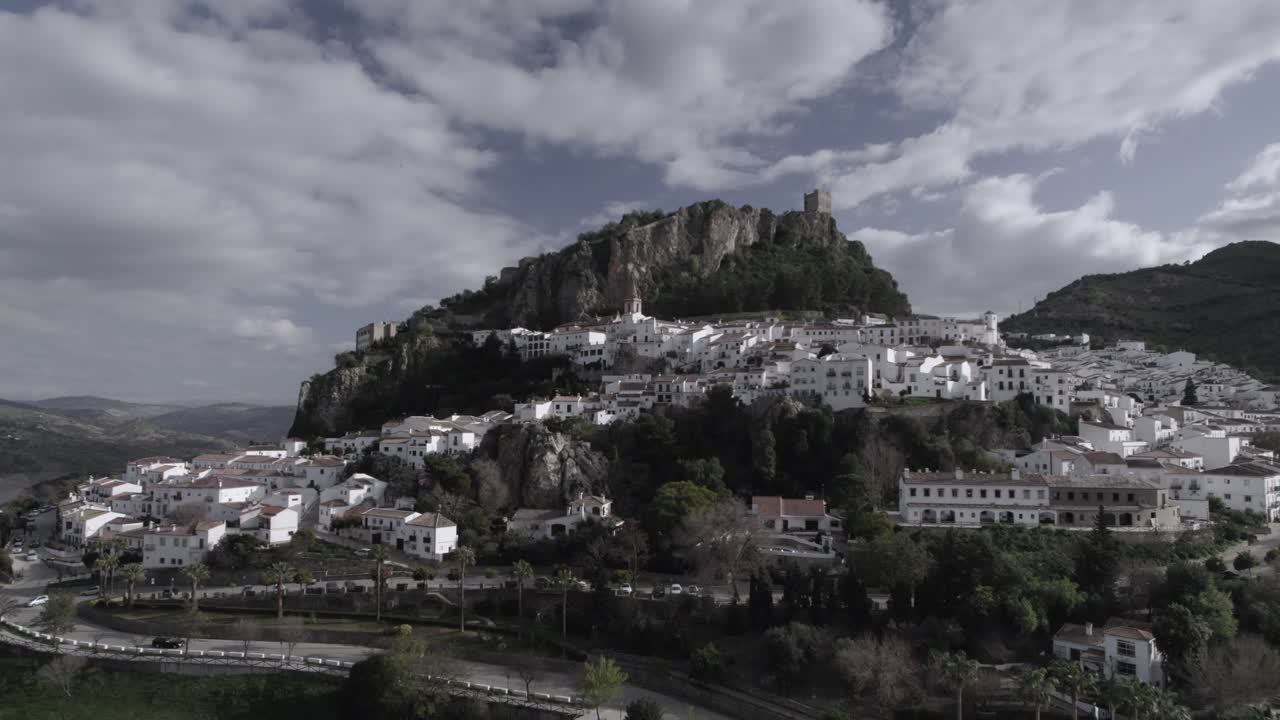 Low-altitude frontal 4K drone shot of Zahara de la Sierra, Spain, filmed with a DJI at 30fps. A cinematic view of the charming village with its historic castle in the background.