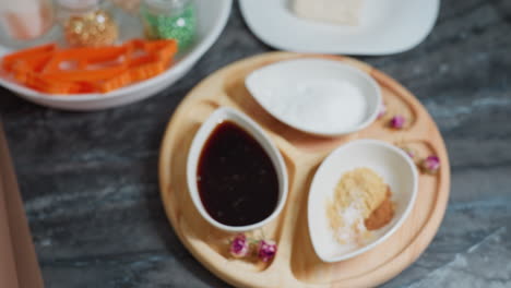목판 위에 향신료, 설탕 및 소스와 함께 세라 그에 있는 커피의 클로즈업, 작은 분홍색 꽃이 장식적인 터치를 추가하고, 베이킹 재료와 쿠키 커터가 배경에 배열되어 있습니다.