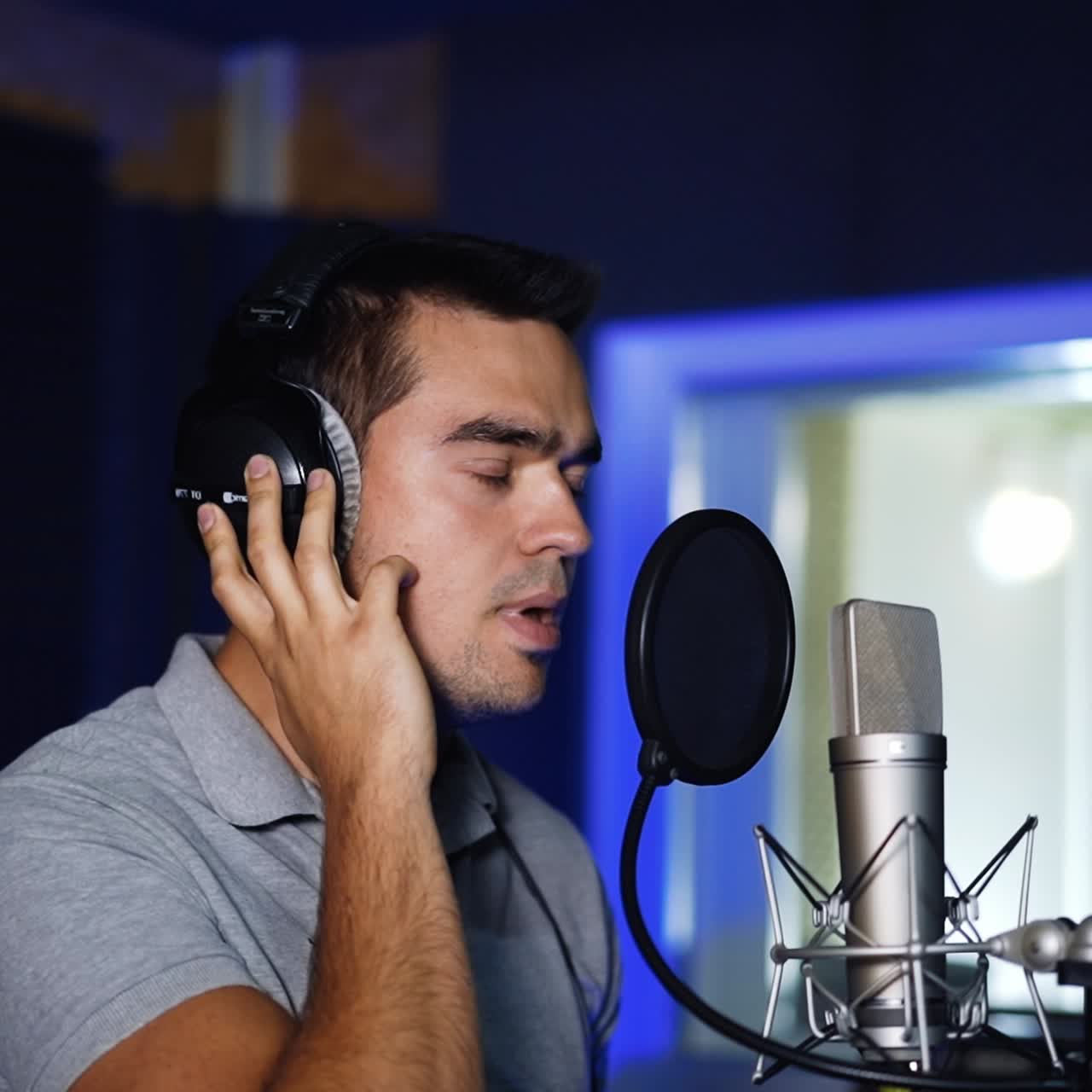 Caucasian singer wearing headphones holding them with his hands sings in front of professional microphone. Music studio song recording