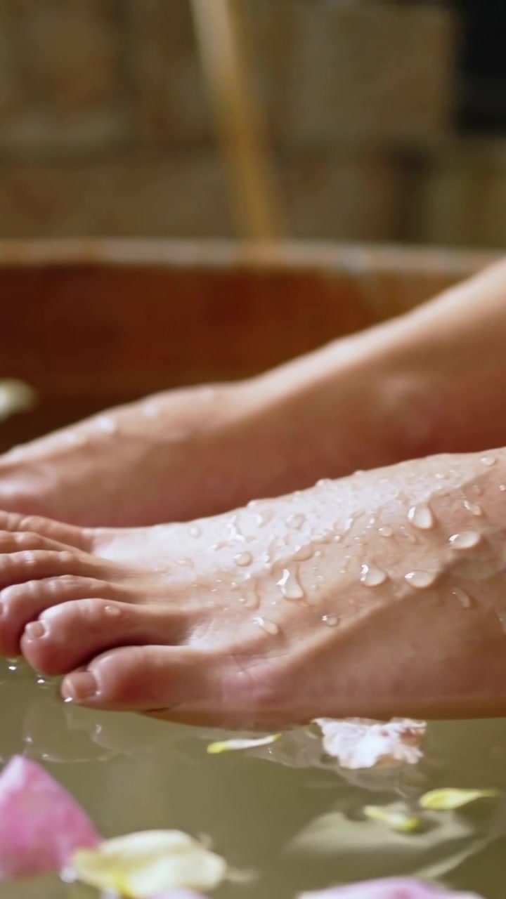 Video verticale: Telecamera panoramica che segue gambe e piedi che si muovono verso una vasca con petali per rilassarsi.