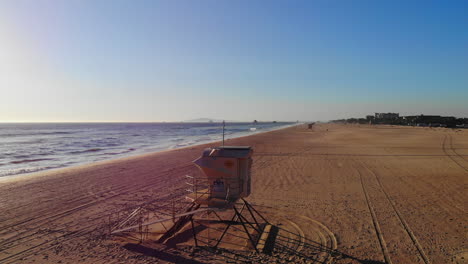 Orbitando-La-Torre-De-Salvavidas-Vacía-Con-Una-Hermosa-Puesta-De-Sol-En-El-Océano-Y-Luego-Volar-Para-Surfear-En-La-Playa-De-Huntington,-En-El-Sur-De-California,-Con-Un-Dron-Aéreo-De-4k-Dji