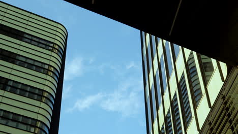 skyscrapers with curved and linear designs against a blue sky, framed by shadows